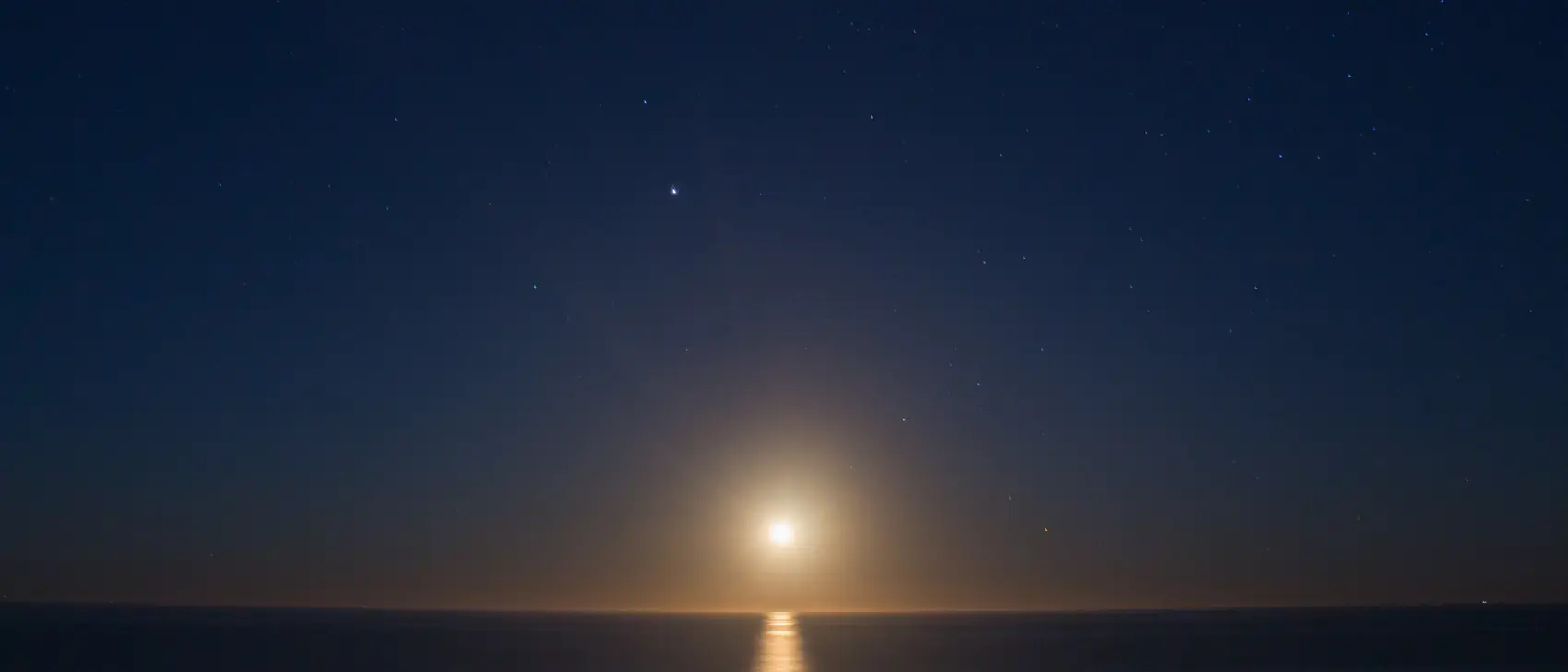 The moon over a calm sea, its reflection drawing a line of light