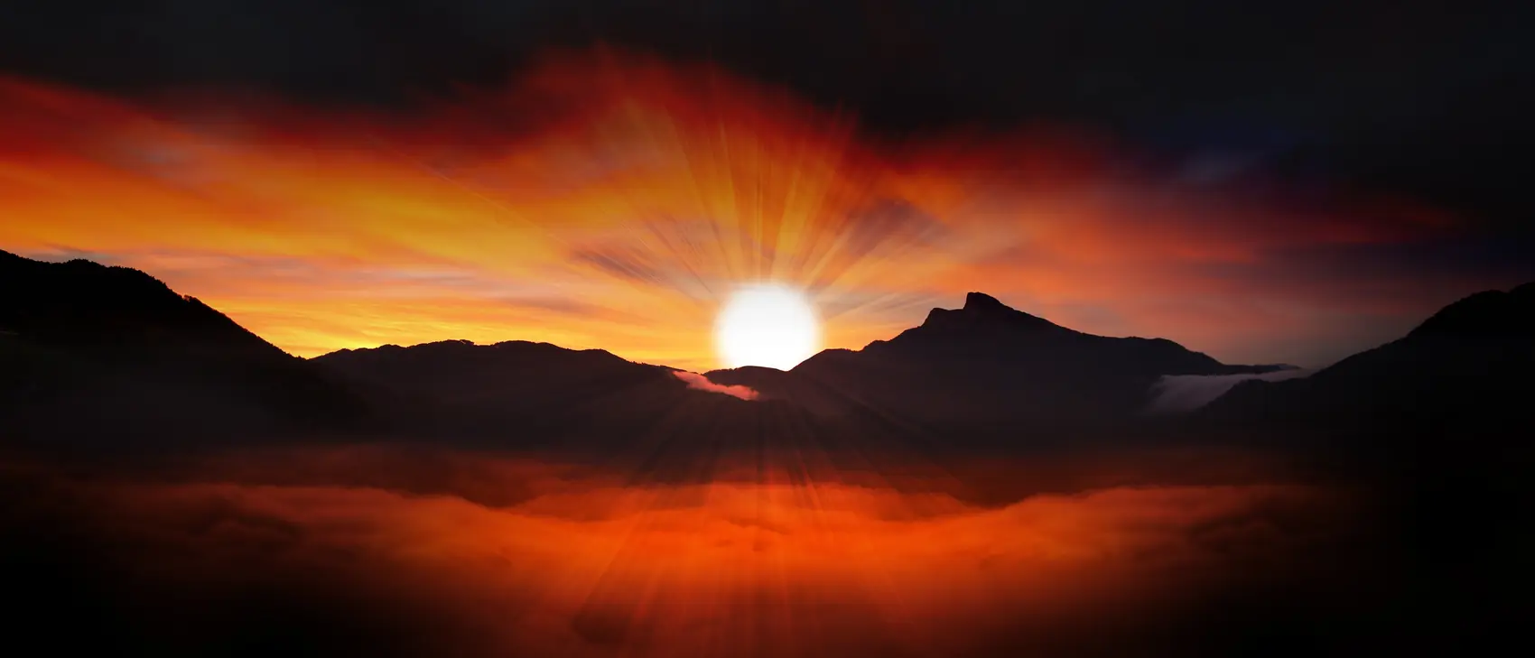 Dawn breaking over dark mountains, with mist in the valley