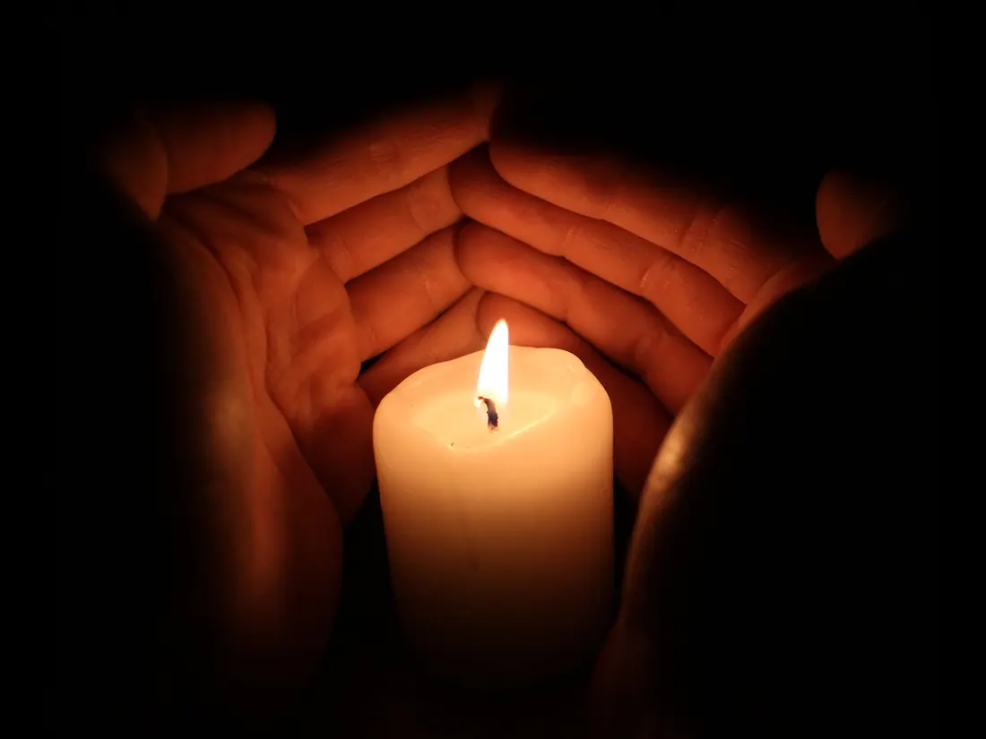 Two hands sheltering a candle flame in the dark